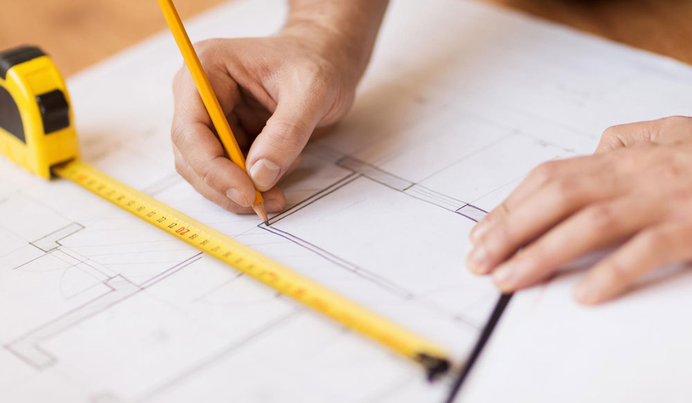 Deux mains, une règle et un mètre, en train de tracer un plan